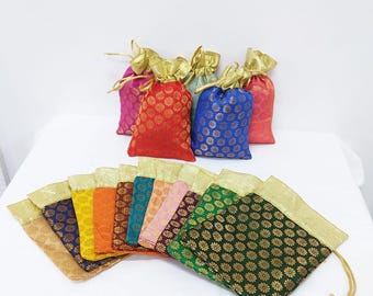 Könnte beinhalten: Eine Sammlung farbenfroher Geschenkbeutel mit Kordelzug. Die Beutel bestehen aus gemustertem Stoff in verschiedenen Farben, darunter Rot, Blau und Grün, mit goldenen Akzenten. Die Beutel sind auf einer weißen Oberfläche angeordnet.
