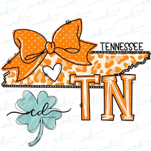 Puede incluir: Lazo naranja y blanco con lunares sobre un contorno de leopardo del estado de Tennessee con las letras TN en naranja. Un pequeño trébol de cuatro hojas verde se encuentra en la esquina inferior izquierda.
