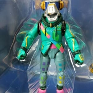 Puede incluir: Una figura de acción verde y azul con una cabeza grande y un casco. La figura tiene un diseño colorido con un patrón rosa, amarillo y azul. La figura lleva una chaqueta verde y pantalones azules.