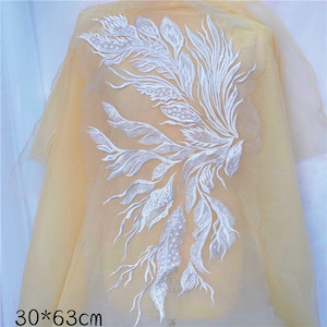 May include: White lace applique with a floral design, measuring 30 by 63 centimetres. The applique is on a sheer, light yellow fabric.