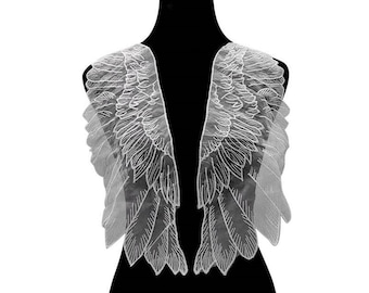 May include: White lace angel wings with a delicate, intricate design. The wings are attached to a black mannequin, creating a dramatic and ethereal look.