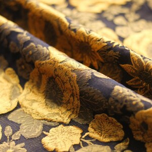 May include: Close-up of a dark blue fabric with a gold floral pattern. The fabric has a textured, raised design.