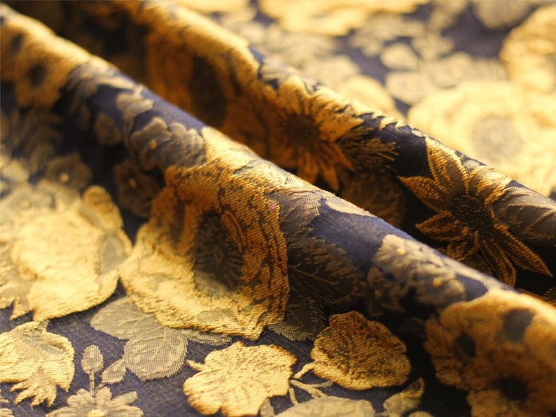 May include: Close-up of a dark blue fabric with a gold floral pattern. The fabric has a textured, raised design.