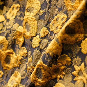 May include: Close-up of a fabric with a textured floral pattern. The fabric is black with gold-colored flowers.