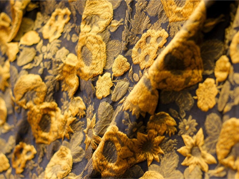 May include: Close-up of a fabric with a textured floral pattern. The fabric is black with gold-colored flowers.