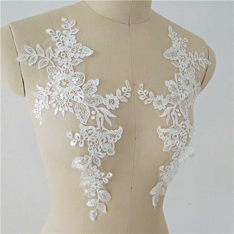 May include: Two white lace appliques with floral designs. The appliques are on a white mannequin.