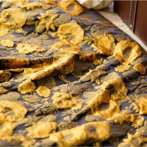 May include: A close-up of a fabric with a gold floral pattern on a dark blue background. The fabric is textured and has a slightly wrinkled appearance.