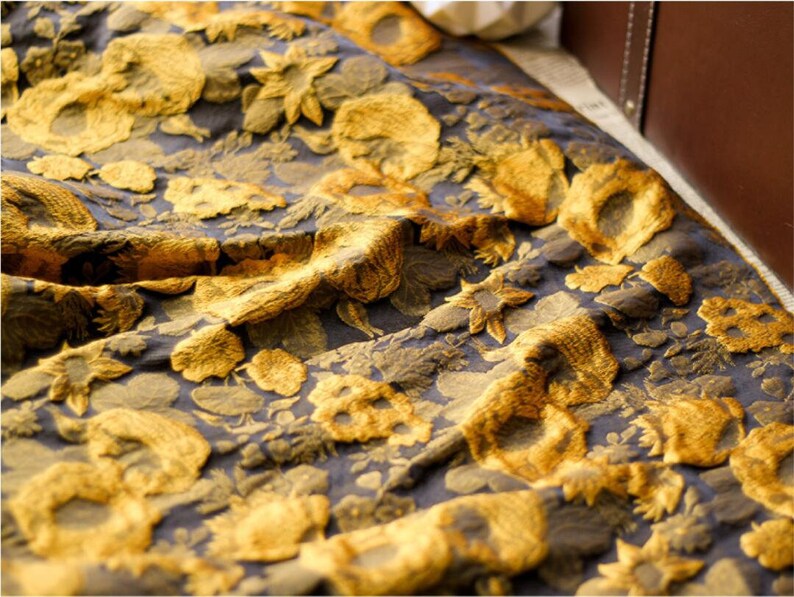 May include: A close-up of a fabric with a gold floral pattern on a dark blue background. The fabric is textured and has a slightly wrinkled appearance.