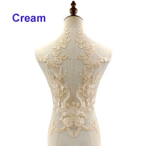 May include: Cream coloured lace applique with floral designs. The applique is displayed on a white dress form.