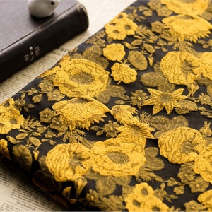 May include: Black fabric with a gold floral pattern. The fabric has a raised texture, giving it a 3D effect.