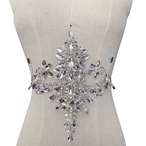 May include: A large, silver rhinestone embellishment in a teardrop shape. The embellishment is made of many small rhinestones that are sewn together to create a decorative design.