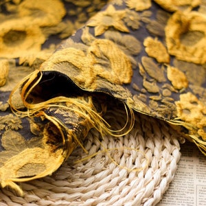 May include: Close-up of a gold and black fabric with a floral pattern. The fabric is folded and draped over a woven basket.