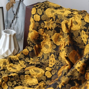 May include: Black fabric with a gold floral pattern. The fabric features a repeating design of large, stylized flowers and leaves.