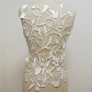 May include: White floral lace applique with delicate flowers and leaves. This lace applique is perfect for adding a touch of elegance to any garment.