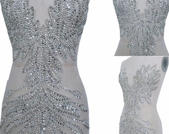May include: A large, silver, crystal-embellished applique for clothing. The applique is shaped like a pair of wings with a pointed center.