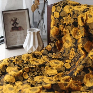 May include: Black fabric with a gold floral pattern. The fabric features a large-scale floral design with intricate details. The fabric is soft and luxurious, perfect for upholstery or drapery.