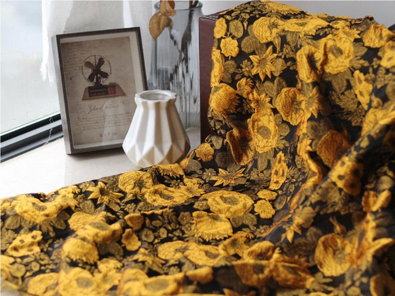 May include: Black fabric with a gold floral pattern. The fabric features a large-scale floral design with intricate details. The fabric is soft and luxurious, perfect for upholstery or drapery.