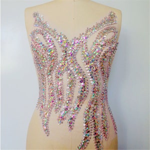 Può includere: Una grande applicazione di strass iridescente a forma di fiore. L'applicazione è realizzata con strass trasparenti con un effetto arcobaleno.