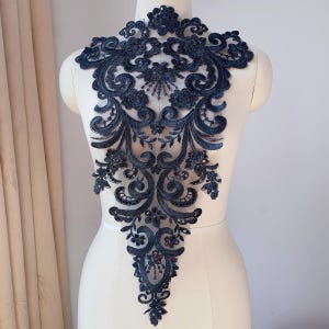 May include: Black lace applique with a floral design and sequins. The applique is shaped like a teardrop and is perfect for adding a touch of elegance to any garment.