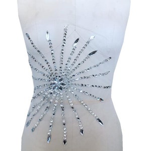May include: A silver rhinestone embellishment in the shape of a starburst. The embellishment is made of small, round rhinestones and larger, oval rhinestones.