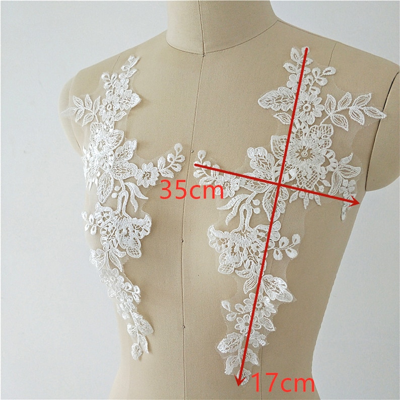 May include: Two white lace appliques with floral designs. The applique on the right measures 17 inches by 35 inches.