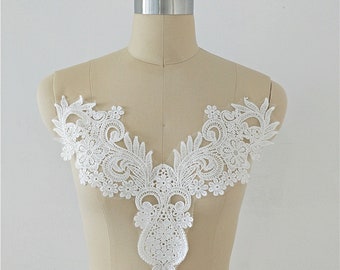 Può includere: Applique in pizzo bianco con un delicato motivo floreale. L'applique ha una scollatura a V e un fondo a punta.