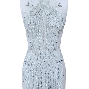 May include: A white beaded applique with a fringe design. The applique is made of small, clear beads and has a delicate, feminine look.