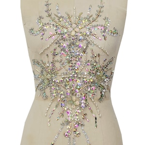 May include: A large, ornate, iridescent rhinestone applique with a floral design. The applique is made of clear, silver, and pink rhinestones and is perfect for adding a touch of sparkle to any garment.