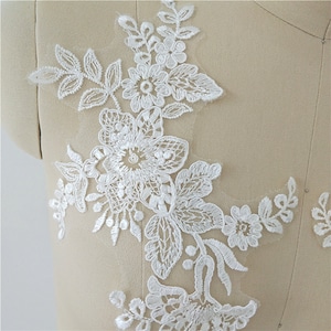 May include: White lace applique with floral designs. The applique features delicate flowers and leaves, perfect for adding a touch of elegance to clothing or crafts.