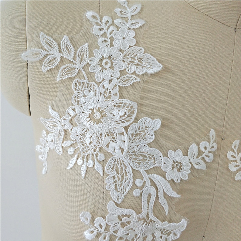 May include: White lace applique with floral designs. The applique features delicate flowers and leaves, perfect for adding a touch of elegance to clothing or crafts.