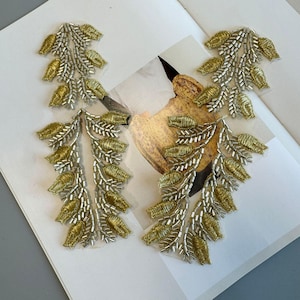 May include: Four decorative leaf-shaped appliques. Each applique features gold-colored embroidered leaves and silver-colored beaded stems. The appliques are arranged on a white surface with a printed design.