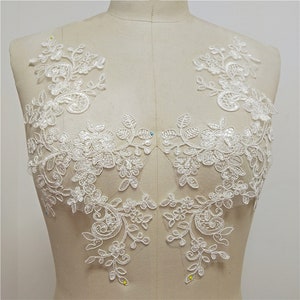 May include: Two white lace appliques with floral designs, perfect for adding a touch of elegance to wedding dresses, bridal accessories, or other craft projects.