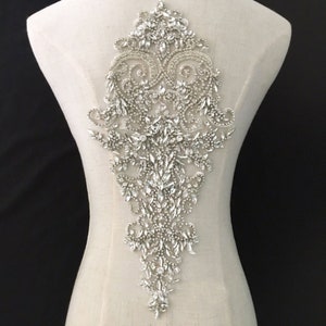 Può includere: Una grande applique argentata decorata con cristalli con un motivo floreale. L'applique è perfetta per aggiungere un tocco di brillantezza agli abiti da sposa, agli abiti da sera o ad altri abiti per occasioni speciali.