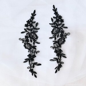 May include: Two black floral lace appliques. Each applique features a detailed design of flowers and leaves. The appliques are symmetrical and are set against a white background. These appliques are suitable for various craft projects.