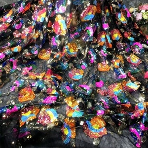 May include: Black mesh fabric with colourful sequin flowers. The sequins are iridescent and create a shimmering effect.