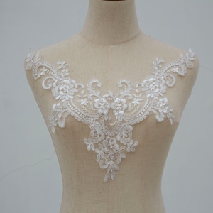 Puede incluir: Aplique de encaje blanco con un diseño floral. El encaje es delicado e intrincado, con pequeñas flores y hojas. Este aplique sería perfecto para agregar un toque de elegancia a un vestido de novia, un vestido de novia u otra prenda para una ocasión especial.