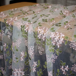 Könnte beinhalten: Weißer, durchsichtiger Stoff mit einem gestickten Blumenmuster in Rosa und Grün.
