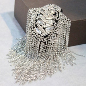 May include: A silver rhinestone and chain fringe embellishment. The embellishment is shaped like a leaf and has a long fringe of chains with rhinestones.