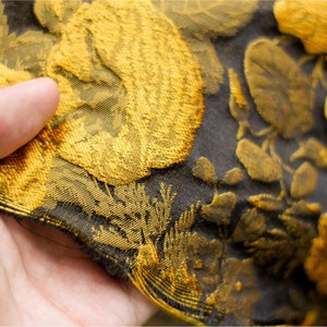 May include: Close-up of a black fabric with a gold floral pattern. The fabric has a textured, woven look.