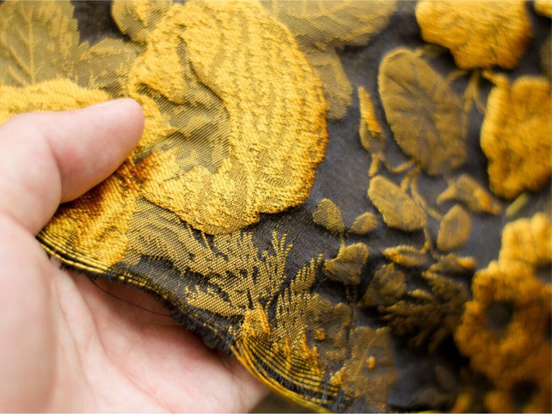 May include: Close-up of a black fabric with a gold floral pattern. The fabric has a textured, woven look.