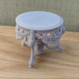 May include: A small, white, round table with intricate carvings and three legs. The table is made of a smooth, white material and has a delicate, ornate design.