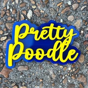 以下が含まれることがあります： 「Pretty Poodle」という文字が書かれた、青と黄色の看板。文字は筆記体で書かれています。