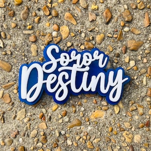 May include: Blue and white acrylic sign with the text "Soror Destiny" in a cursive font.