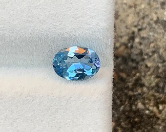 May include: An oval-shaped, light blue gemstone with cut facets, displayed on a white surface. The gemstone reflects light, highlighting its clarity and colour. The gem is likely a precious or semi-precious stone, suitable for jewellery.