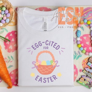 May include: A white t-shirt with the words "EGG-CITED FOR EASTER" in purple and orange. The design includes a basket filled with colorful eggs and floral accents, perfect for Easter celebrations.