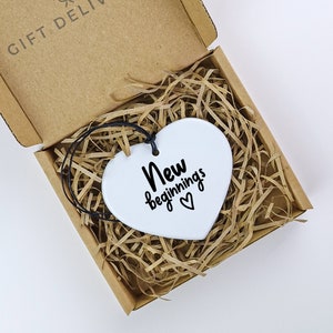 May include: White ceramic heart-shaped ornament with black text that reads "New beginnings" and a small heart symbol.