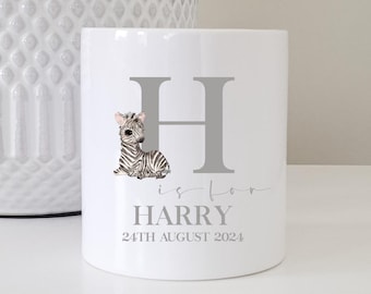 Puede incluir: Hucha de cerámica blanca con una letra H gris y una ilustración de cebra. El texto "H is for HARRY 24TH AUGUST 2024" está impreso en la caja.