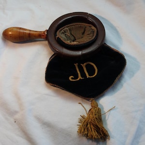 May include: A wooden brush with a handle and a black velvet bag with a gold tassel and the initials "JD" embroidered on it.