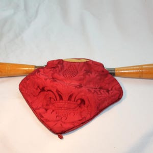 May include: A red velvet pouch with a floral pattern and two wooden handles. The pouch is closed and the handles are extended on either side.