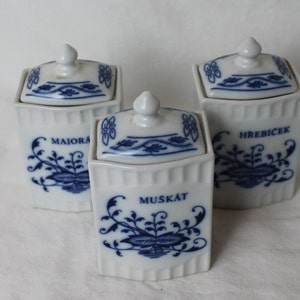 May include: Three white ceramic spice jars with blue and white floral designs and lids. The jars are labelled "Majorana", "Muskat", and "Hrebicek".